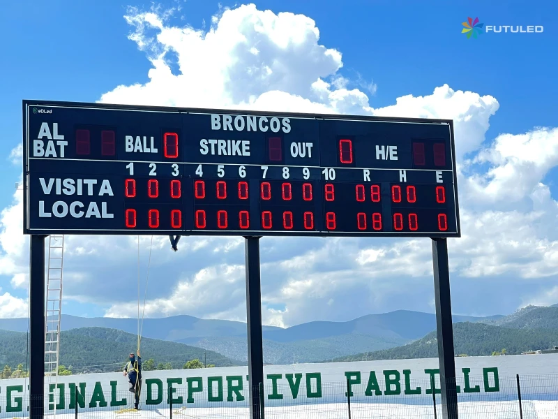 Técnico realizando mantenimiento a un gran marcador de béisbol electrónico marca Futuled en el Centro Regional Deportivo Pablillo, mostrando estadísticas del equipo Broncos.
