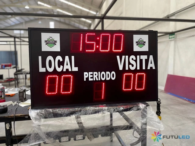 Marcador Deportivo Digital LED - Futuled Marcador deportivo digital LED de la marca Futuled sobre una mesa de taller, mostrando indicadores de tiempo a 15:00, puntaje de local y visita en 00, y el periodo 1.