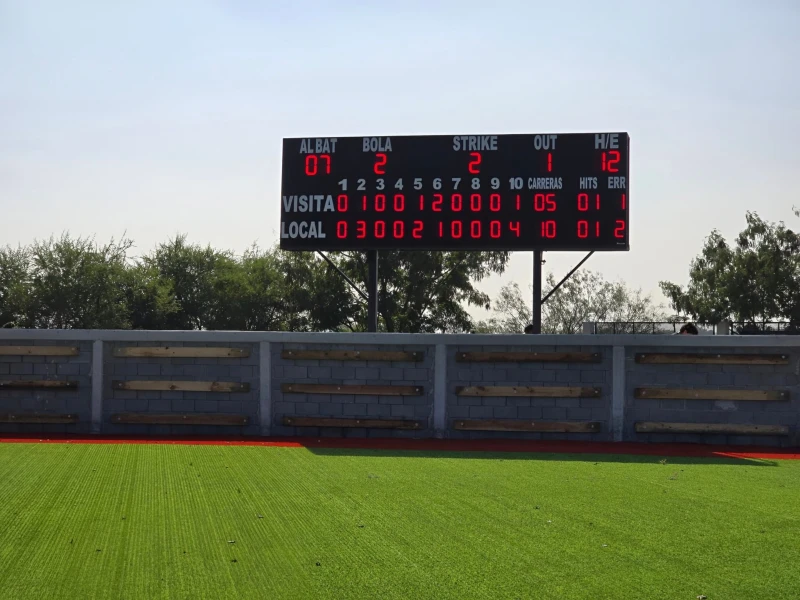 Marcador LED de Béisbol para Exteriores - Futuled Marcador electrónico LED para béisbol en exteriores instalado en un campo de césped artificial, mostrando entradas, carreras, strikes y bolas